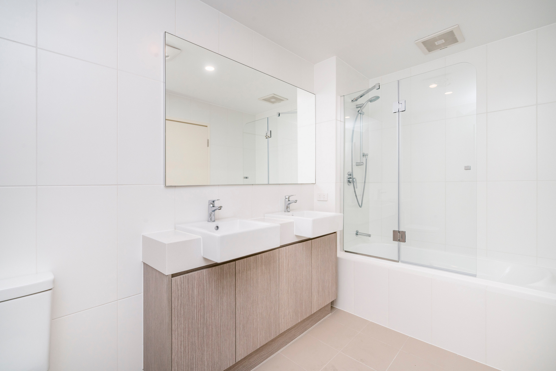 Modern minimal bathroom interior with wooden cabinets and glass shower screen.